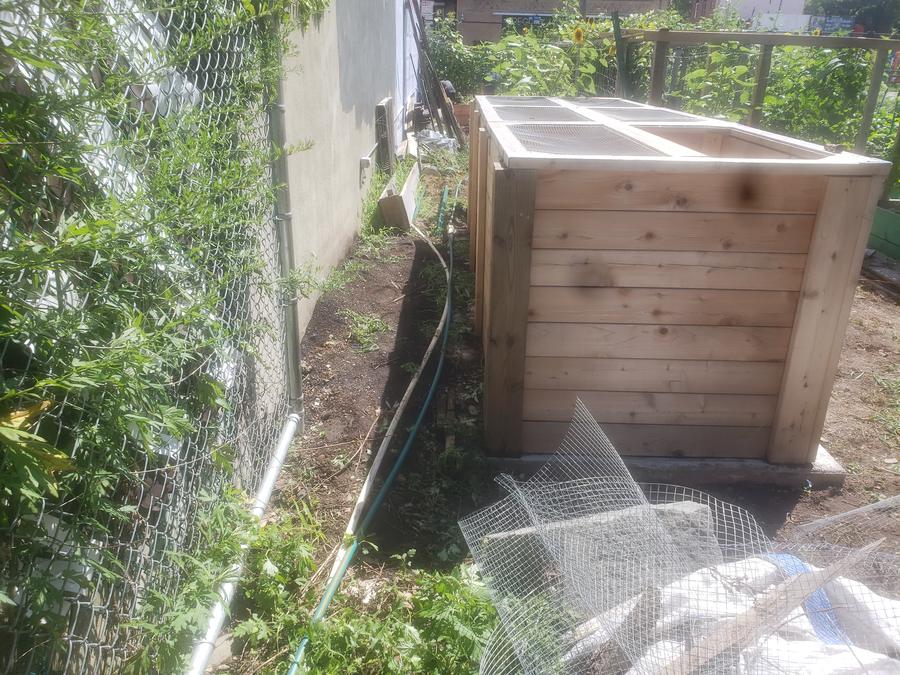 Finished multi-bay composting bins with hinged mesh lids at a community garden