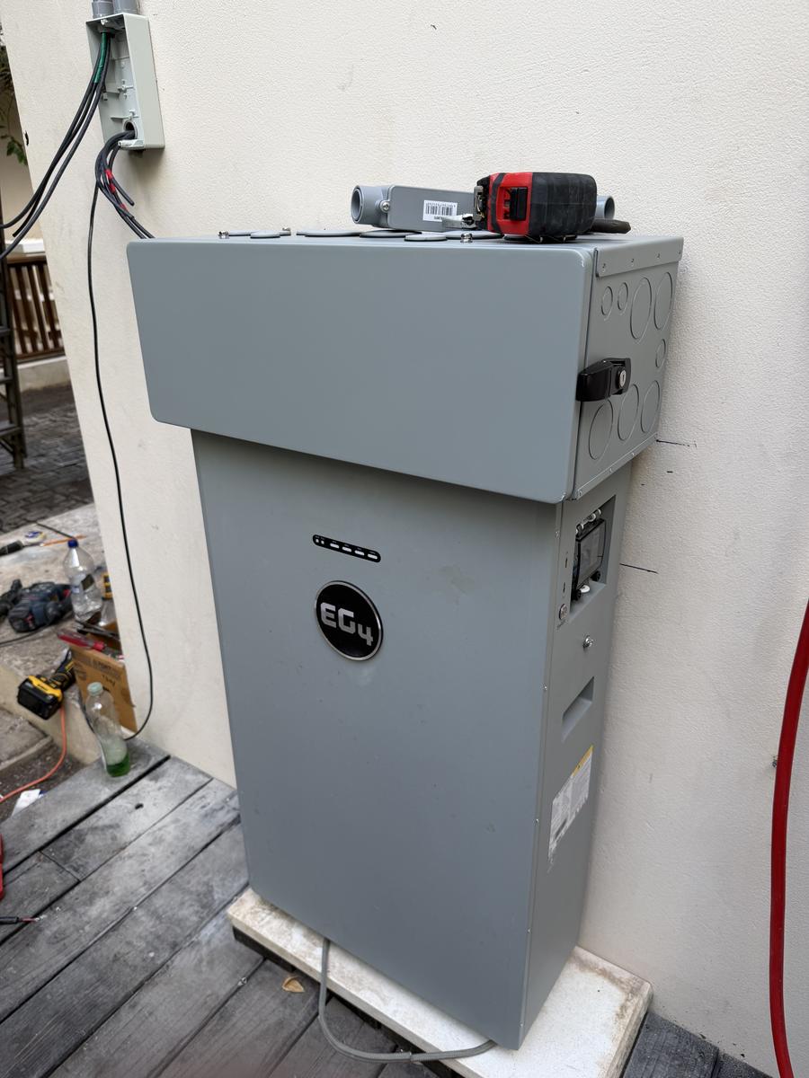 Finished battery storage cabinet with conduit fittings on top, mounted against an exterior wall