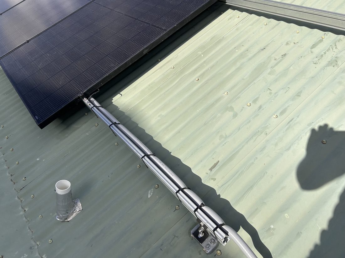 Close-up of solar panel mounting rail and conduit run on a metal roof